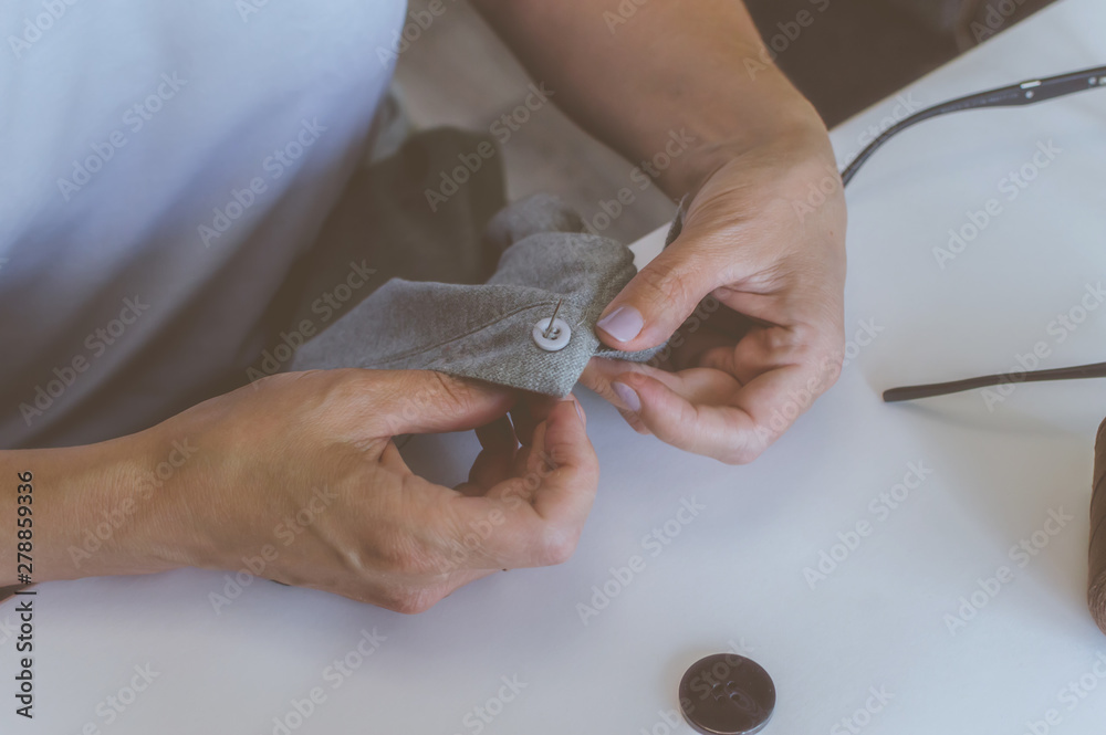 women's hands, a tailor sews clothes at a table on which spools of thread lie