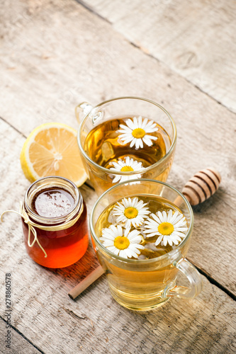 Herbal tea in a glass bowl with camomile flowers, lemon and honey on rustic wooden background, selective focus
