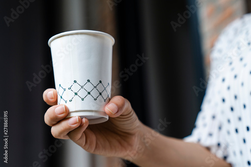Pretty young woman in stylish white cloths holding cup in hands. Warm soft cozy image. Details. Drinking take away coffee. Breakfast on the go. Instagram style toned image