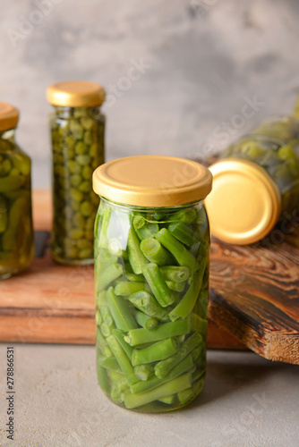 Jar with canned green beans on grey background