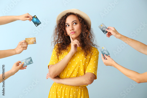 Thoughtful African-American woman and hands with credit cards on color background photo