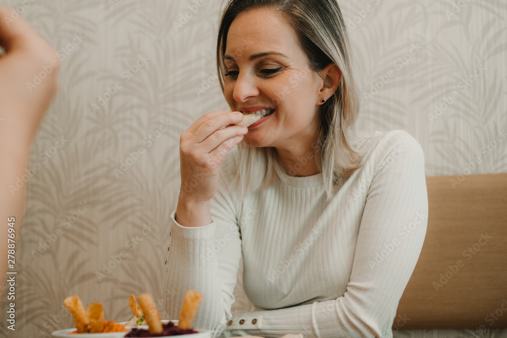 Attractive young woman having lunch with friend and tasting appetizing snack at table Attractive young woman having lunch with friend and tasting appetizing snack at table