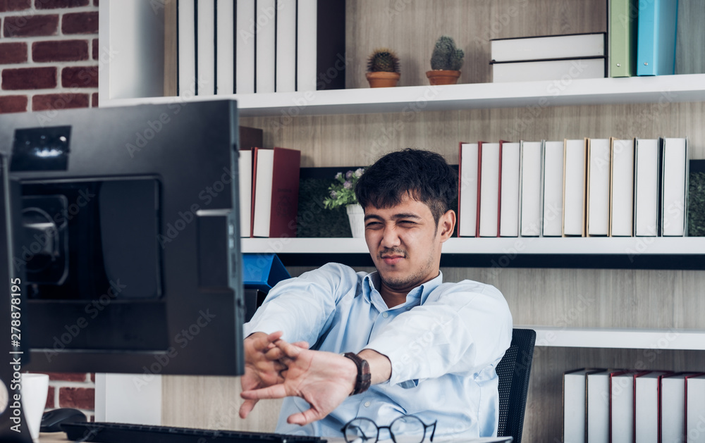 Fototapeta premium Tired asian businessman stretching in front of desktop computer in modern office after working all day.working hard and get burn out syndrome concept.exercise when overworked at table