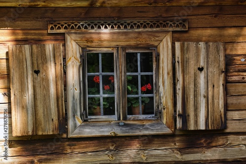 Drewniany dom z drewnianymi okiennicami, ozdobami i pelargoniami w oknach