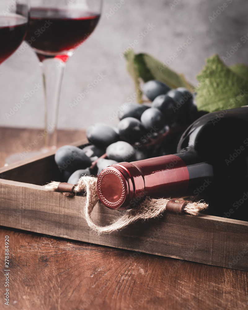 Obraz premium Bottle of red wine with ripe grapes on wooden tray .