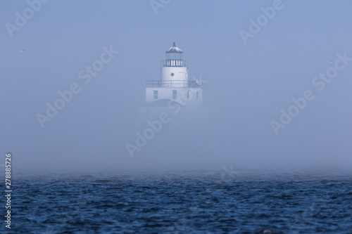 The thick fog partially obscures the lighthouse on Lake Michigan