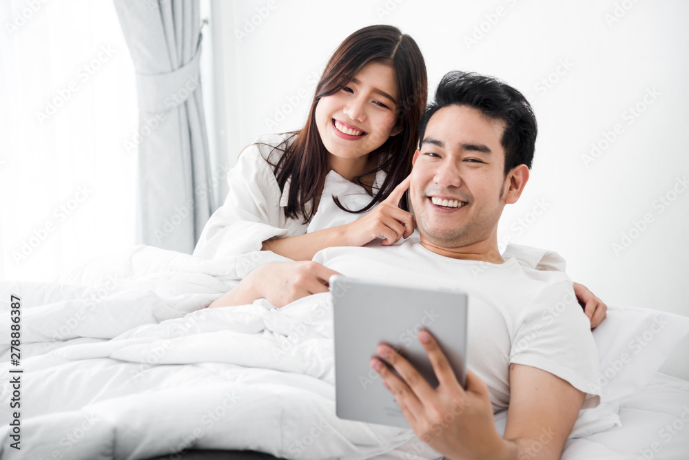 Happy Asian couple using laptop and tablet together on bed at home, lifestyle concept. Happy Asian couple using laptop and tablet together on bed at home, lifestyle concept.