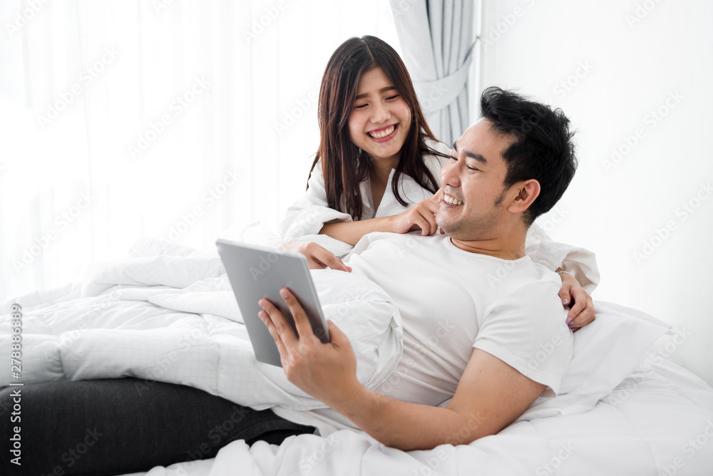 Happy Asian couple using laptop and tablet together on bed at home, lifestyle concept. Happy Asian couple using laptop and tablet together on bed at home, lifestyle concept.