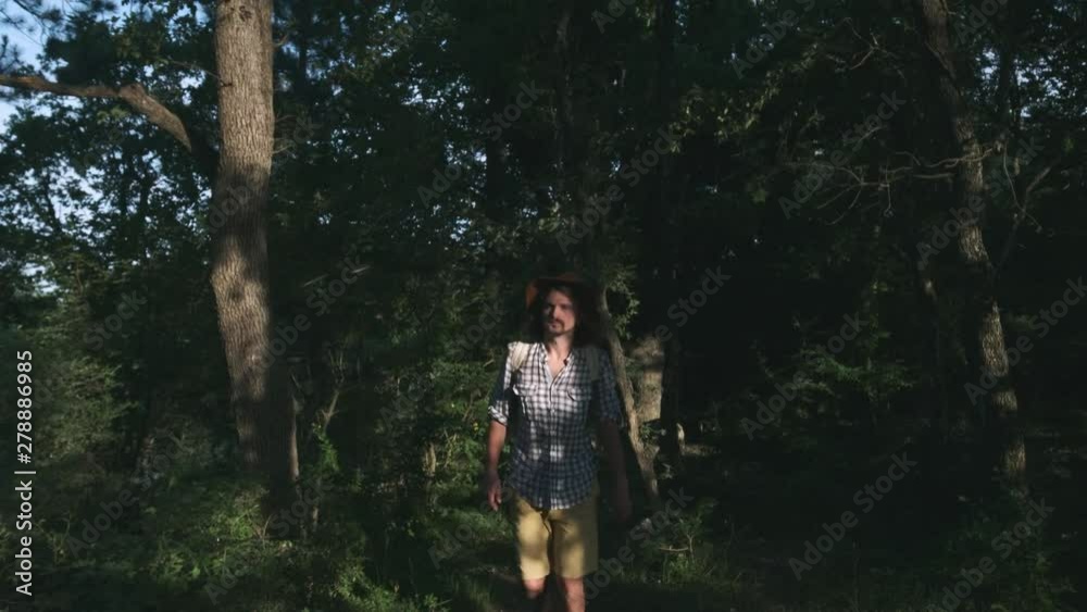 A young peasant walking in the woods. Hiker hiking in forest at sunset. Active lifestyle. Wearing a checkered shirt and a traveler's hat. Backpack traveler. Hiking travel concept. A young peasant walking in the woods. Hiker hiking in forest at sunset. Active lifestyle. Wearing a checkered shirt and a traveler's hat. Backpack traveler. Hiking travel concept.
