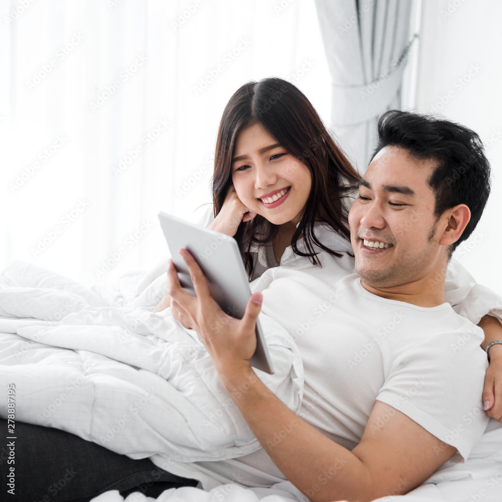 Happy Asian couple using laptop and tablet together on bed at home, lifestyle concept. Happy Asian couple using laptop and tablet together on bed at home, lifestyle concept.