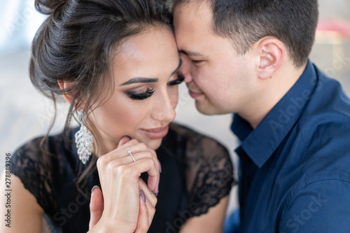 Close up portrait of couple in love. guy and girl touch their foreheads. Beautiful evening make-up and hairstyle for girl