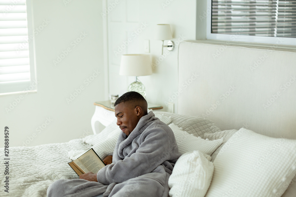 Man reading a book while lying on bed in bedroom at comfortable home Man reading a book while lying on bed in bedroom at comfortable home