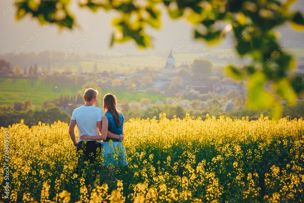 Man and woman in love looking at beautiful spring rural landscape. Gold and yellow sunset colors