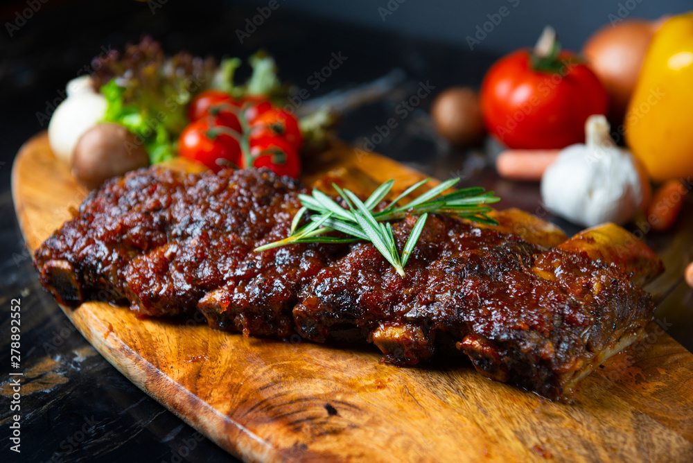 BBQ beef ribs steak served with a hot chili pepper and fresh tomatoes on an old vintage wooden cutting board