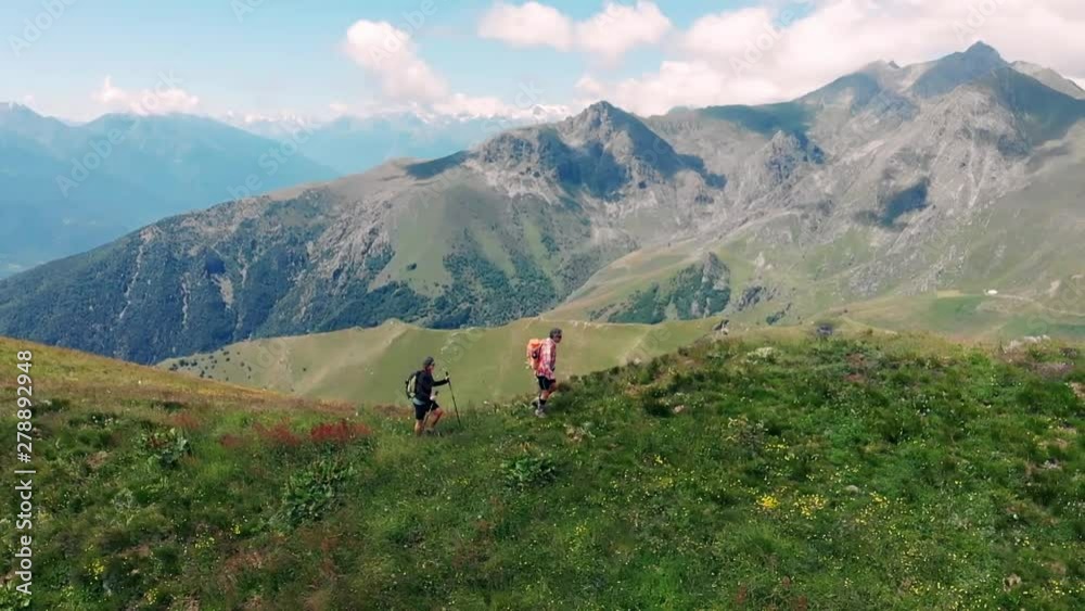Aerial slow motion: couple backpackers hiking on mountain top, scenic landscape. Summer adventures on the Alps. Conquering success mature adult having fun wellbeing fitness Aerial slow motion: couple backpackers hiking on mountain top, scenic landscape. Summer adventures on the Alps. Conquering success mature adult having fun wellbeing fitness