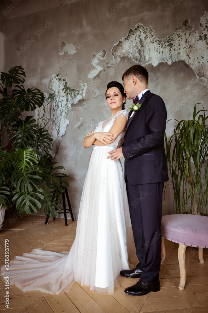 Bride in an elegant dress and groom in a suit on a background of tropical plants