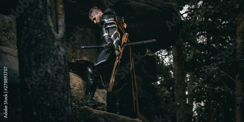 Mystery scarface knight in armor with sword and crossbow in the forest