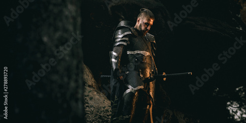 Foto Mystery scarface knight in armor with sword and crossbow in the forest