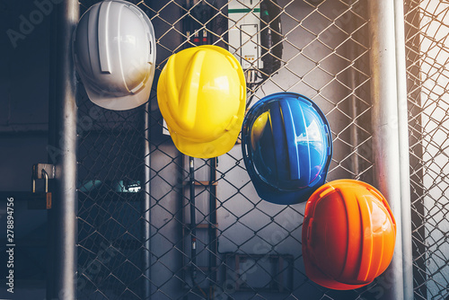 White, yellow, blue and orange helmets that hang on the iron fence at the construction site.