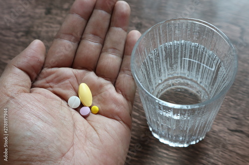 medicine on hand and glass of water on wooden background.