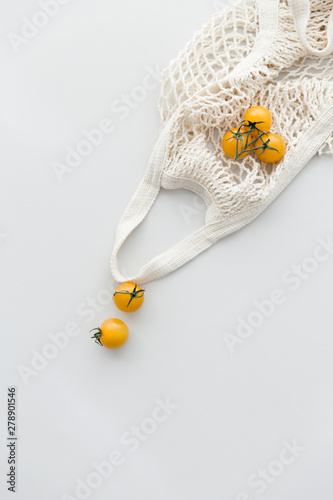 A white natural cotton shopping bag with yellow cherry tomatoes on a light grey surface.