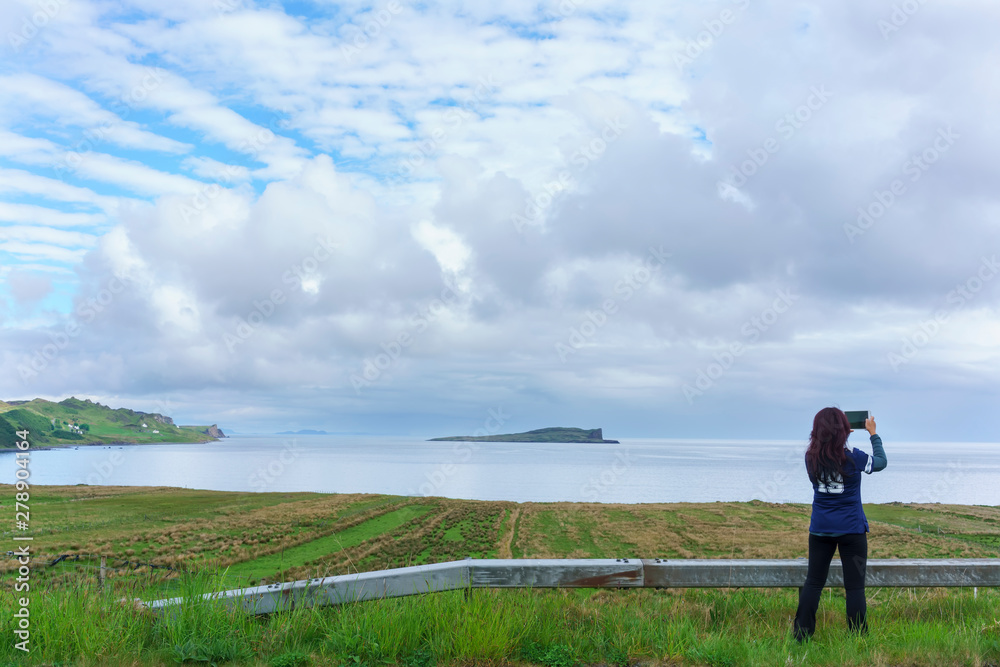 Woman taking picture of beautiful scenery on Isle of Skye in summer , Scotland