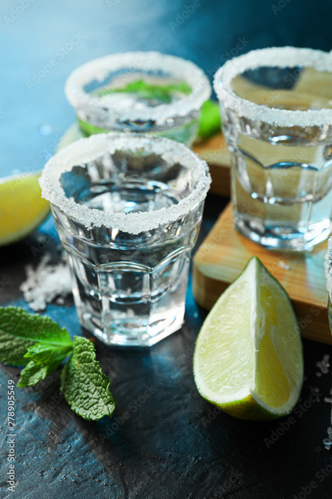 Tequila shots with salt, lime slices and mint on black table with blue light