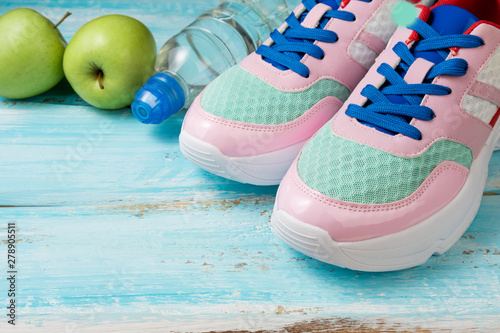 Pink sport shoes, bottle of water and green apples on blue wooden background. Sport, healthy lifestyle, dieting, running concept. Trendy female sport equipment. Copy space