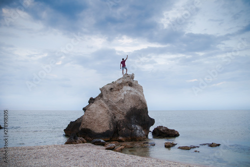 The guy climbed a rock into the sea and raised his arms in a victorious gesture.