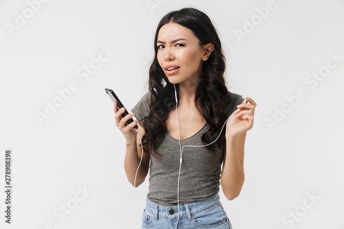 Woman posing isolated over white wall background listening music with earphones using mobile phone.