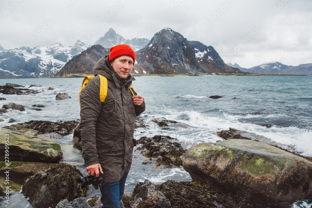 Obraz premium Traveller professional photographer taking nature photo of landscape. Wearing a yellow backpack wearing a red hat standing on rocks against the background of the sea and the mountains