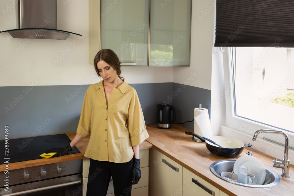 A young woman cleans up in the kitchen, washing dishes. She is tired and not satisfied with the fact that she needs to do it. A young woman cleans up in the kitchen, washing dishes. She is tired and not satisfied with the fact that she needs to do it.
