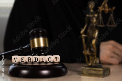 Word VERDICT composed of wooden dices. Wooden gavel and statue of Themis in the background.