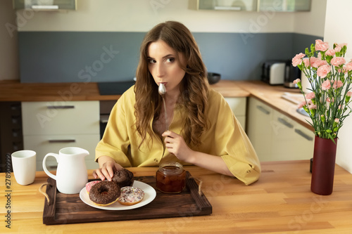 A beautiful young girl with long hair is sitting at home in the kitchen and is planning to have breakfast. For breakfast she has high-calorie, not healthy food. She doubts her decision a little.