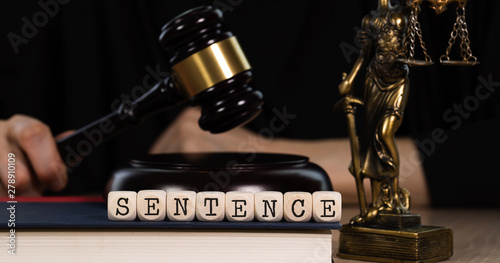 Word SENTENCE composed of wooden dices. Wooden gavel and statue of Themis in the background.