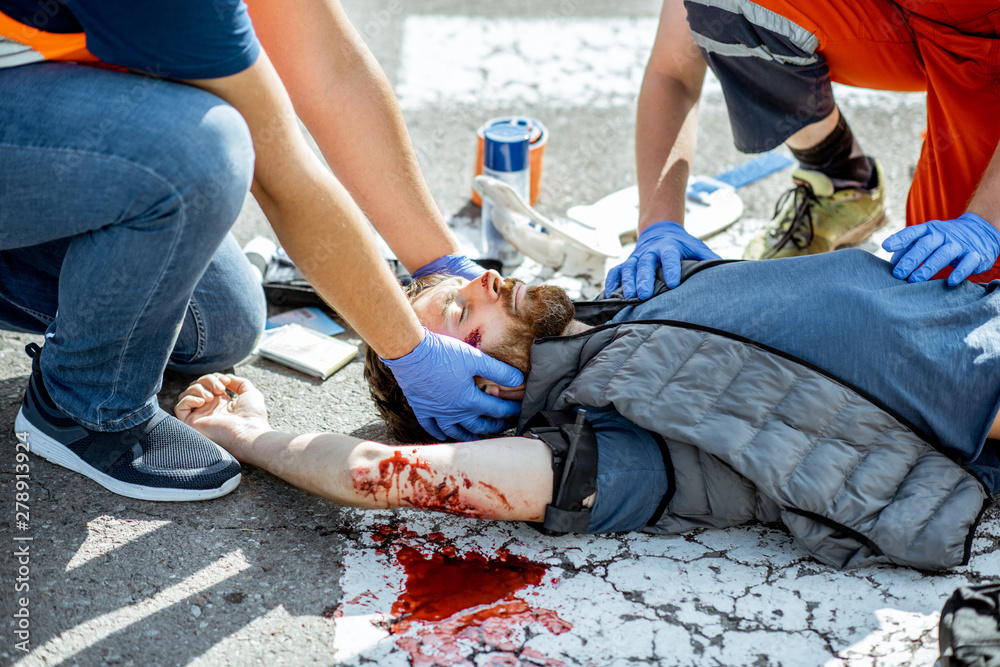 Ambluence workers applying emergency care to the injured bleeding man lying on the pedestrian crossing after the road accident Ambluence workers applying emergency care to the injured bleeding man lying on the pedestrian crossing after the road accident