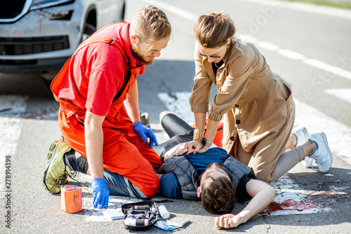 Woman with ambluance worker making artificial respiration to the injured bleeding man lying on the pedestrian crossing after the road accident