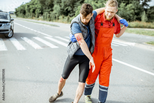 Medic in uniform helping injured man to walk, applying first aid after the road accident