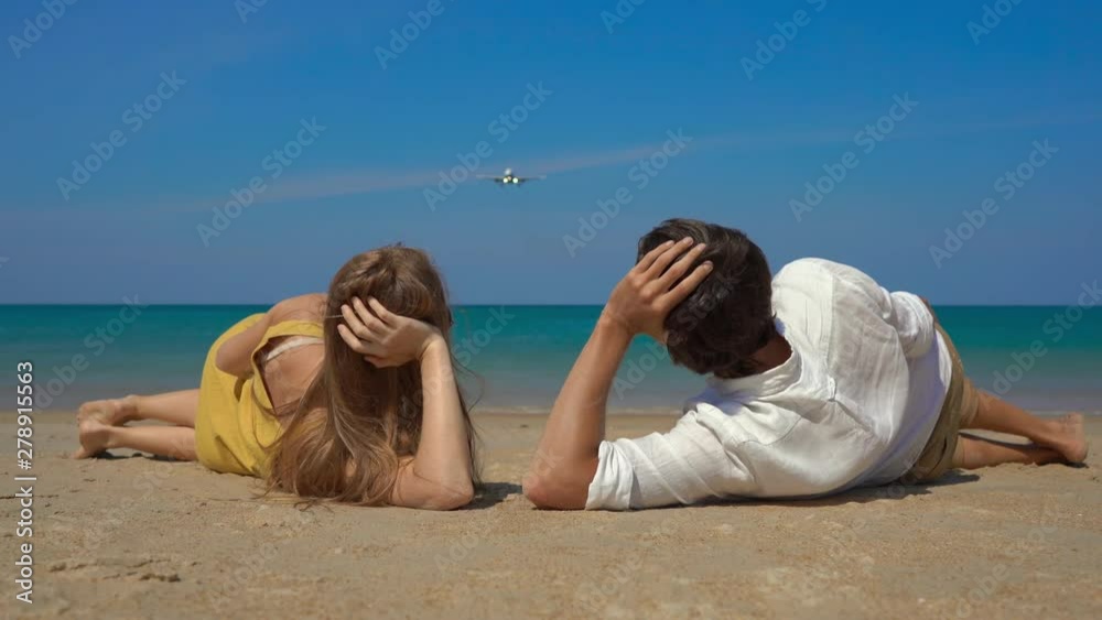 young man and woman laying on a beautiful beach watch a landing airplane young man and woman laying on a beautiful beach watch a landing airplane