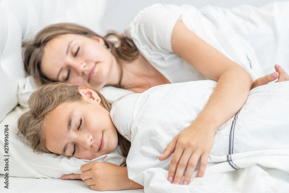 Mom and daughter sleep together on the bed at home Mom and daughter sleep together on the bed at home