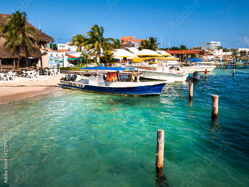 Isle of Ladies or “Isla de Mujeres” is a Mexican island off the tip of the Yucatan Peninsula showing the fishing boats moored on the beach with the clear azure green blue water. 