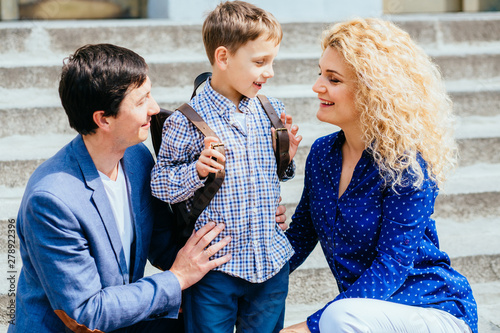 Enjoying family concept. Mother and dad sending their child pupil boy first time studing to school over stairs on background. Parents hugging and say bood bye to son. photo