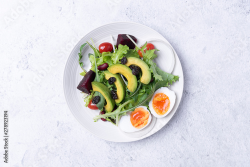 Fresh healthy vegetable salad with egg, tomato, avocado, spinach, lettuce in plate on table background.
