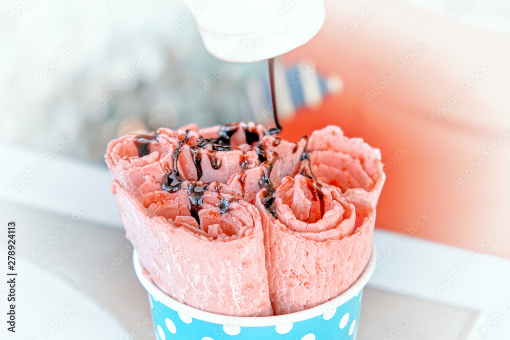 fried rolled ice cream food cooking process closeup view of icecream and  strawberry sweet dessert roll in cup on table background chocolate topping  adding to rolls from bottle for handmade ice-cream foto