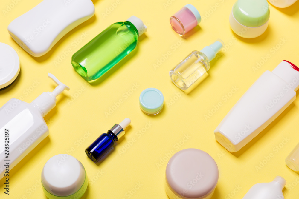 Composition of different sized cosmetic jars and bottles on yellow background. Beauty care concept with copy space Composition of different sized cosmetic jars and bottles on yellow background. Beauty care concept with copy space