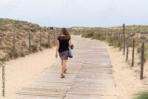 Fototapeta Naklejka Na Ścianę i Meble -  Woman walking on the sandy beach rear view in path wooden