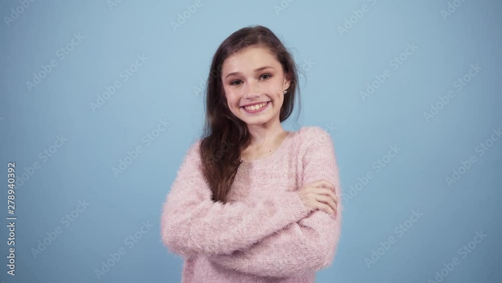 Pretty little model posing in studio isolated on light blue. Brown haired girl looks at camera, smiling, gesturing with OK sign and wink to the camera Pretty little model posing in studio isolated on light blue. Brown haired girl looks at camera, smiling, gesturing with OK sign and wink to the camera