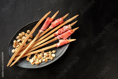 Prosciutto-wrapped Italian grissini with roasted almonds, shot from above on a black background with a place for text