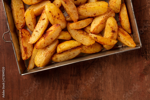 Potato wedges, oven roasted, close-up shot from above in a baking tray on a dark rustic wooden background with a place for text