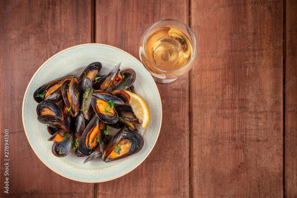 Marinara mussels, moules mariniere, with a glass of white wine, shot from the top on a dark rustic wooden background with a place for text Marinara mussels, moules mariniere, with a glass of white wine, shot from the top on a dark rustic wooden background with a place for text